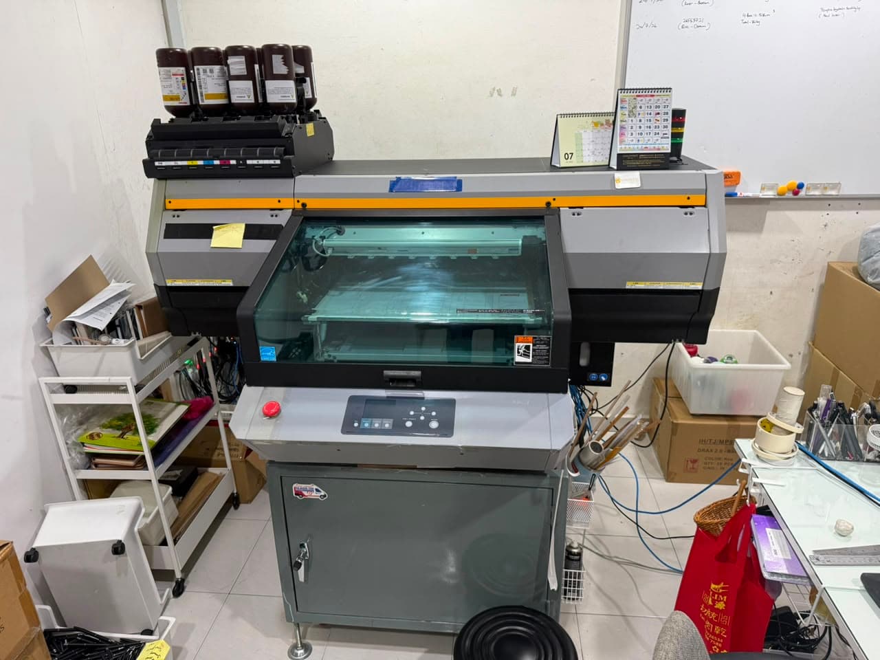 Goldvest's flatbed UV printer in the Penang workshop, ink bottles loaded and a job board on the wall behind it